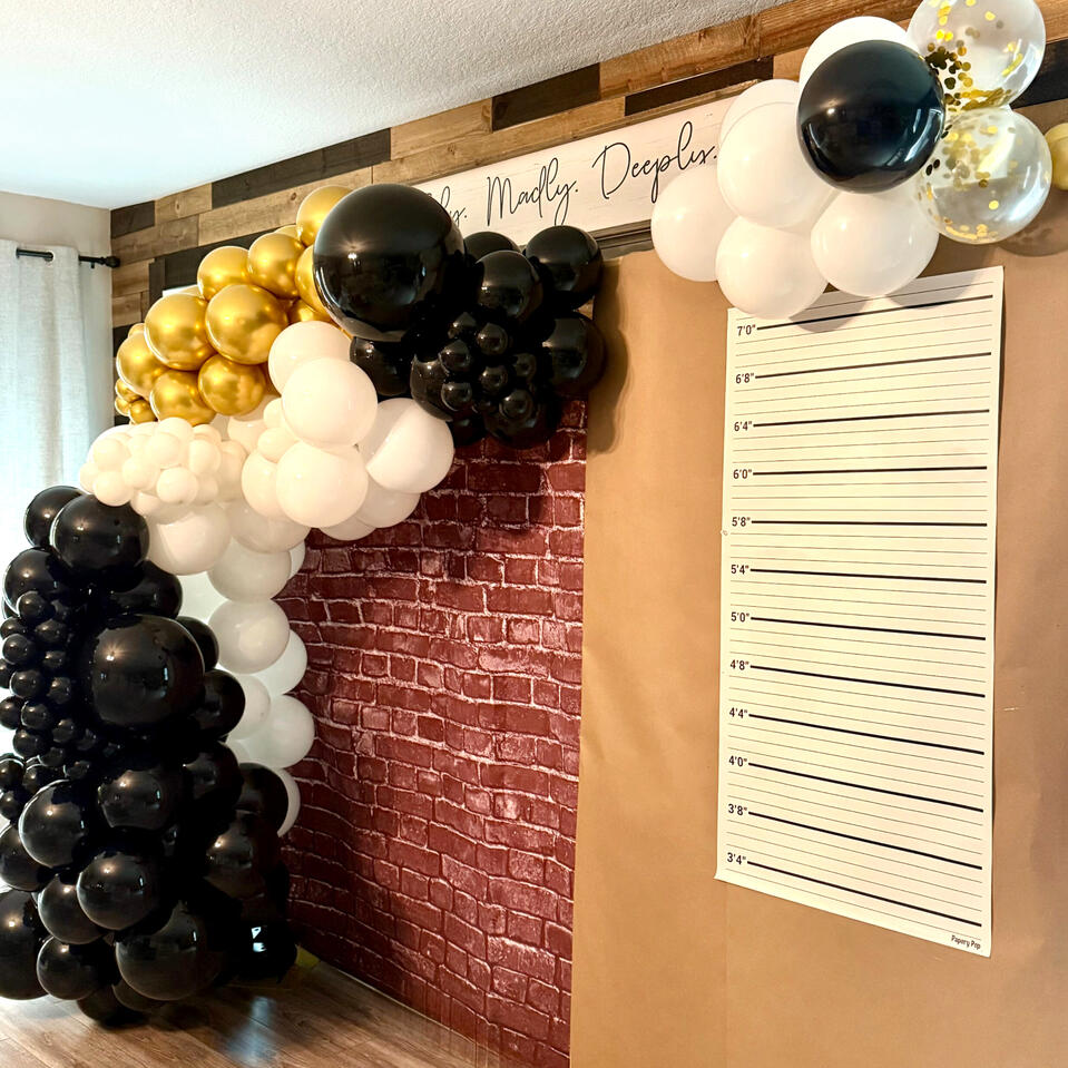 Murder Mystery Party organic balloon garland in black, white, and gold with a mugshot inspired wall graphic