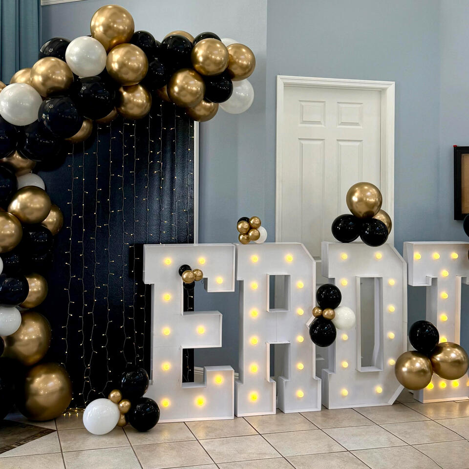 balloon garland setup in black, white, and gold with light up marquee letters