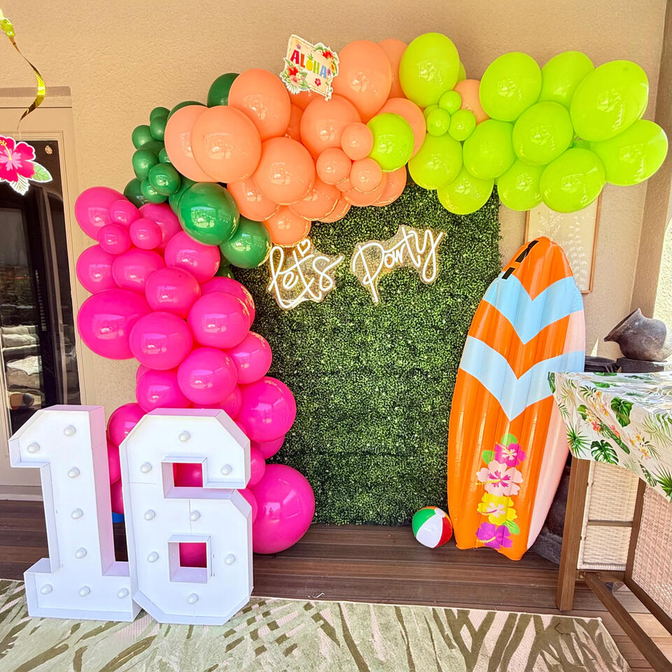 Luau Sweet 16 colorful garland with greenery wall and lighting