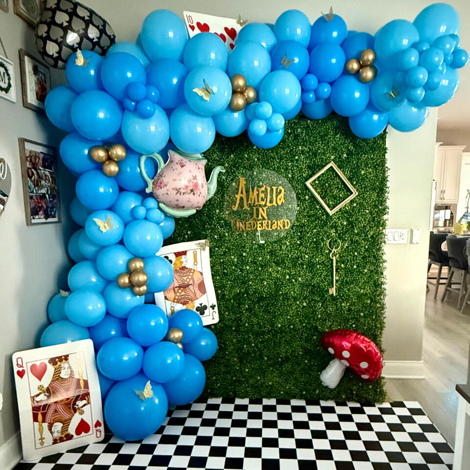 Onederland 1st Birthday Party organic garland feature wall with specialty balloons and custom alice in wonderland themed accents on a greenery backdrop