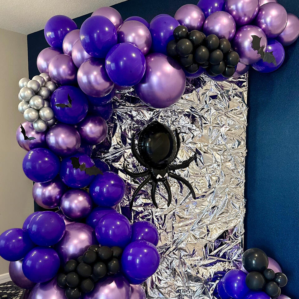 wednesday themed install with an organic garland in black, silver, and purples, a specialty spider balloon, and bat accents