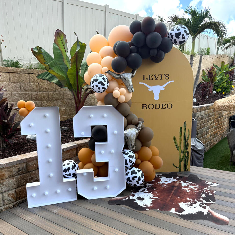 rodeo themed party set up with arches, organic balloon garland, and light up marquee numbers